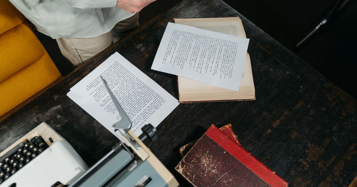 Overhead view of a classic wooden desk with a typewriter, scattered papers, and vintage books.