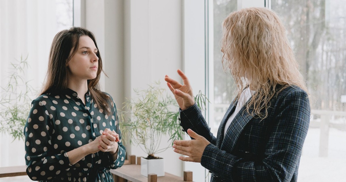 Concentrated young female colleagues in elegant outfits standing near window in light office and discussing project