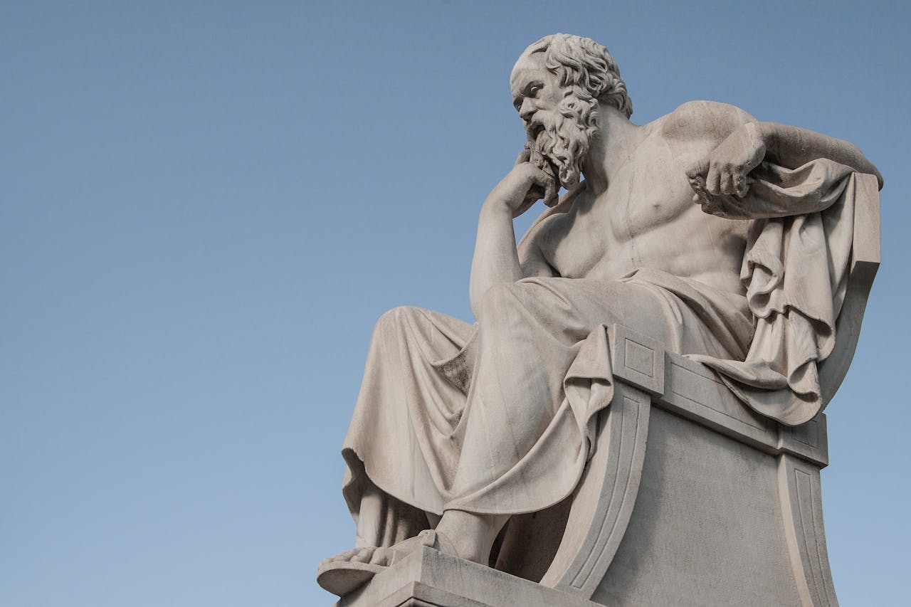 Stone statue of philosopher Socrates sitting in thoughtful pose in Athens, Greece under a clear blue sky