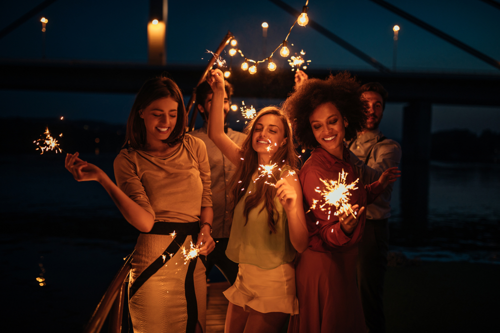 Cropped shot of a group of friends holding sparklers on a boat