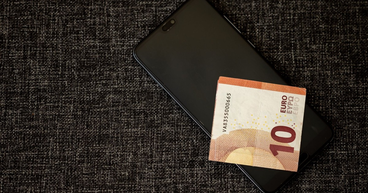 A 10 euro banknote placed on a smartphone on a textured dark fabric background.