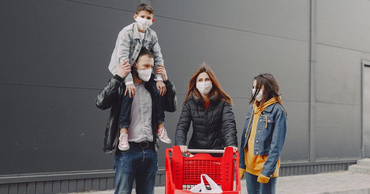 Family in casual clothes with protective masks standing on street with shopping trolley after spending time together in supermarket