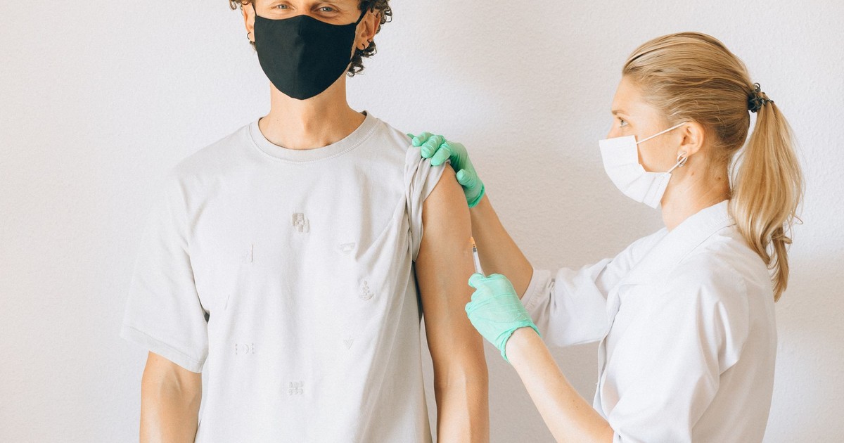 A healthcare worker giving a vaccine injection to a masked man in a clinic.