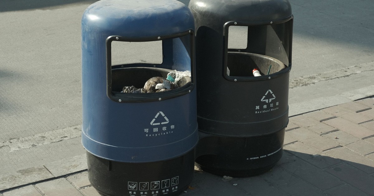 Blue and black recycling and waste bins on a city sidewalk, emphasizing urban waste management.