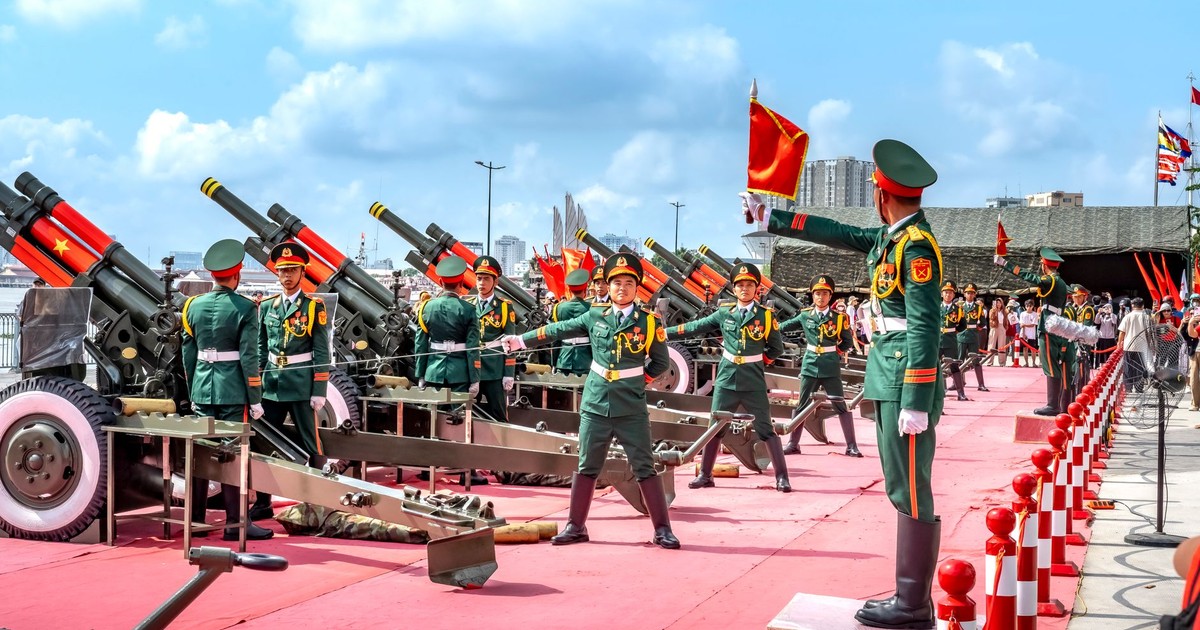 Military parade with soldiers and artillery cannons on display, featuring colorful uniforms and flags.