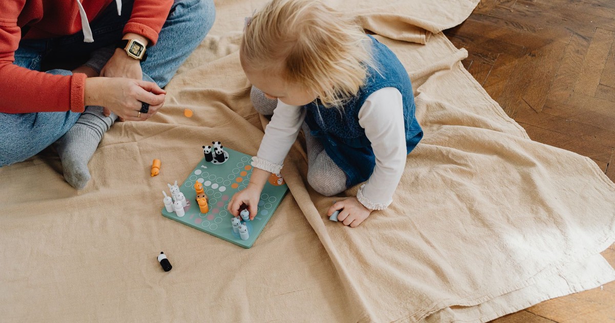 Child playing a board game with an adult on a wooden floor, enjoying indoor activities.