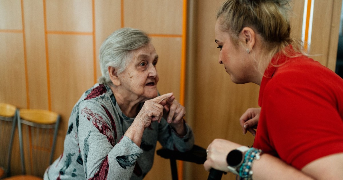 Elderly woman and caregiver in conversation inside a room in Karviná, Česko.