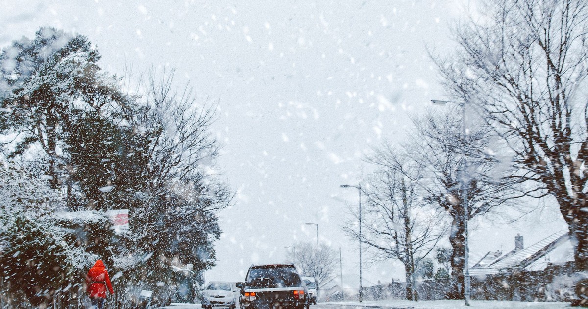 A car driving through a snowy road during a heavy winter storm, capturing a serene winter landscape.