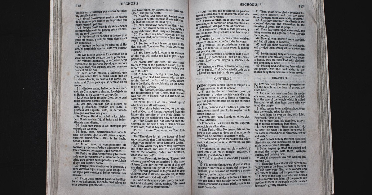 An open Bible displaying chapters of Acts in Spanish and English, photographed from above.