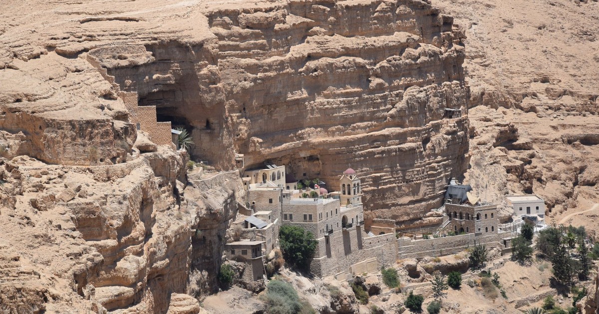 Aerial view of St George's Monastery nestled in the cliffs of Wadi Qelt, illuminated by bright sunlight.