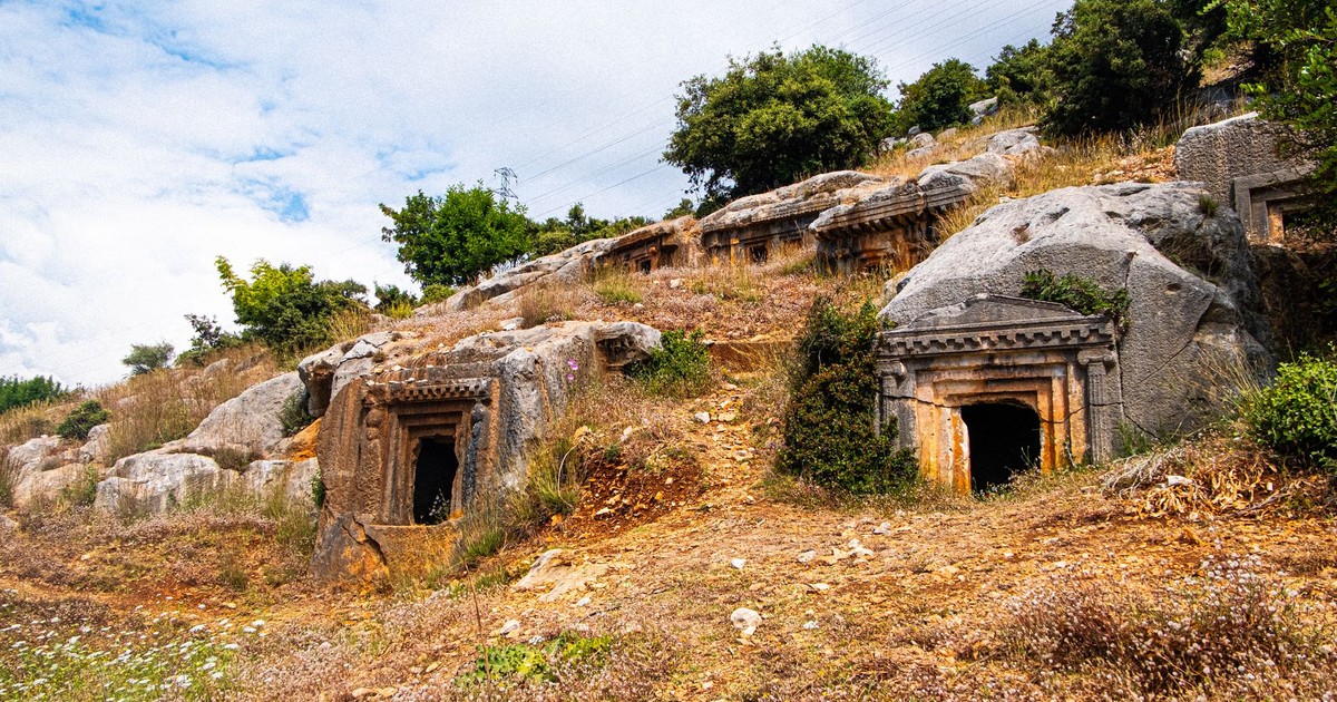 Explore ancient rock-cut tombs nestled in a scenic hillside landscape, captured brilliantly under a clear sky.
