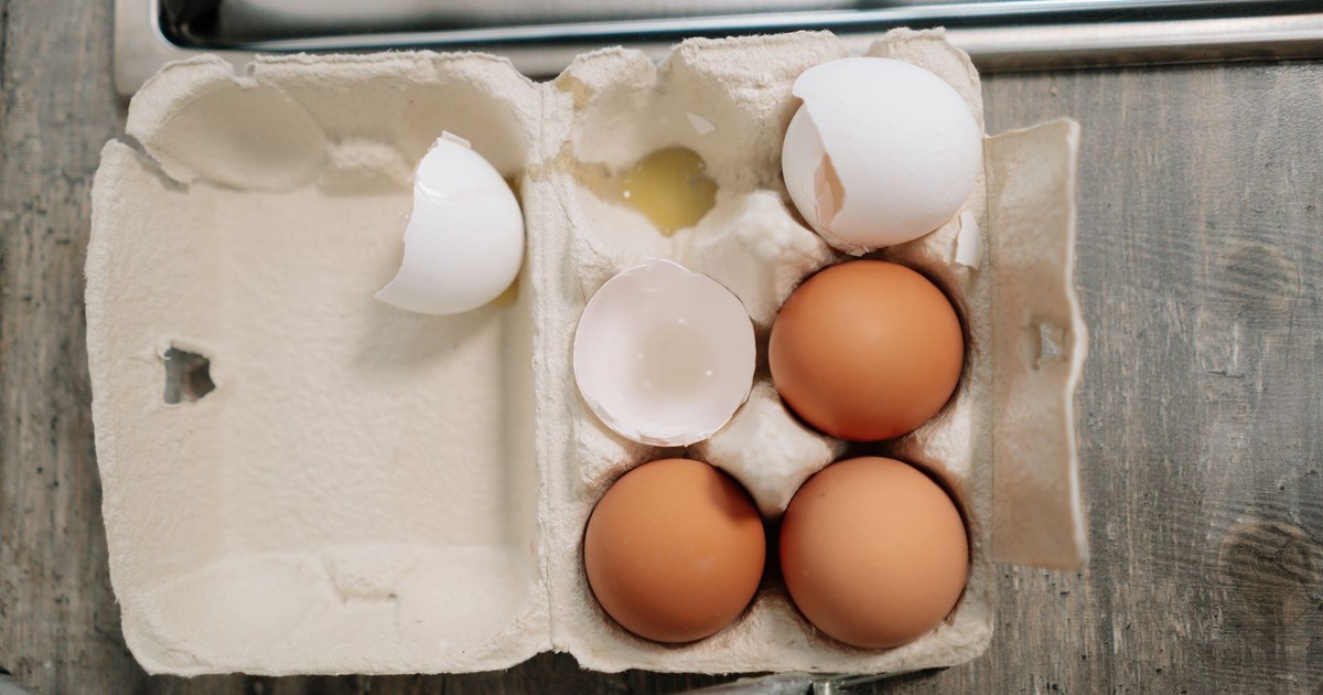 Overhead view of fresh brown and broken white eggs in carton on wooden surface.