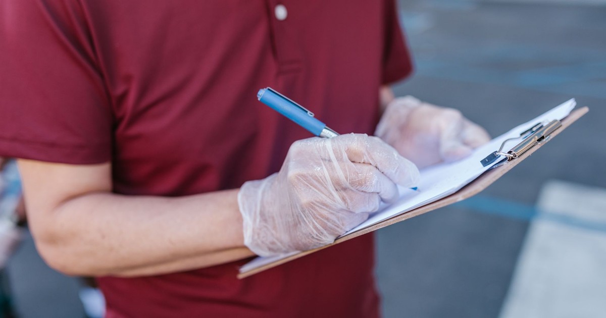 A person wearing gloves writes on a clipboard outdoors in casual attire.