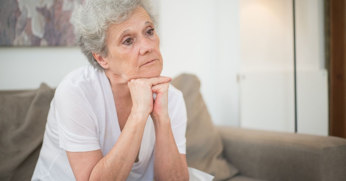 A thoughtful senior woman with gray hair sitting indoors, reflecting.