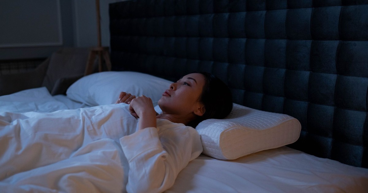 An Asian woman lying awake in bed at night, showing signs of insomnia and sleeplessness.