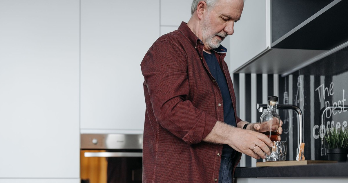 A senior man with gray hair pours a drink in a contemporary indoor kitchen setting.