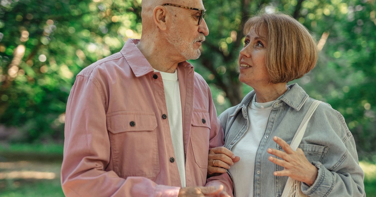 An elderly couple shares a joyful conversation in a vibrant green park setting.
