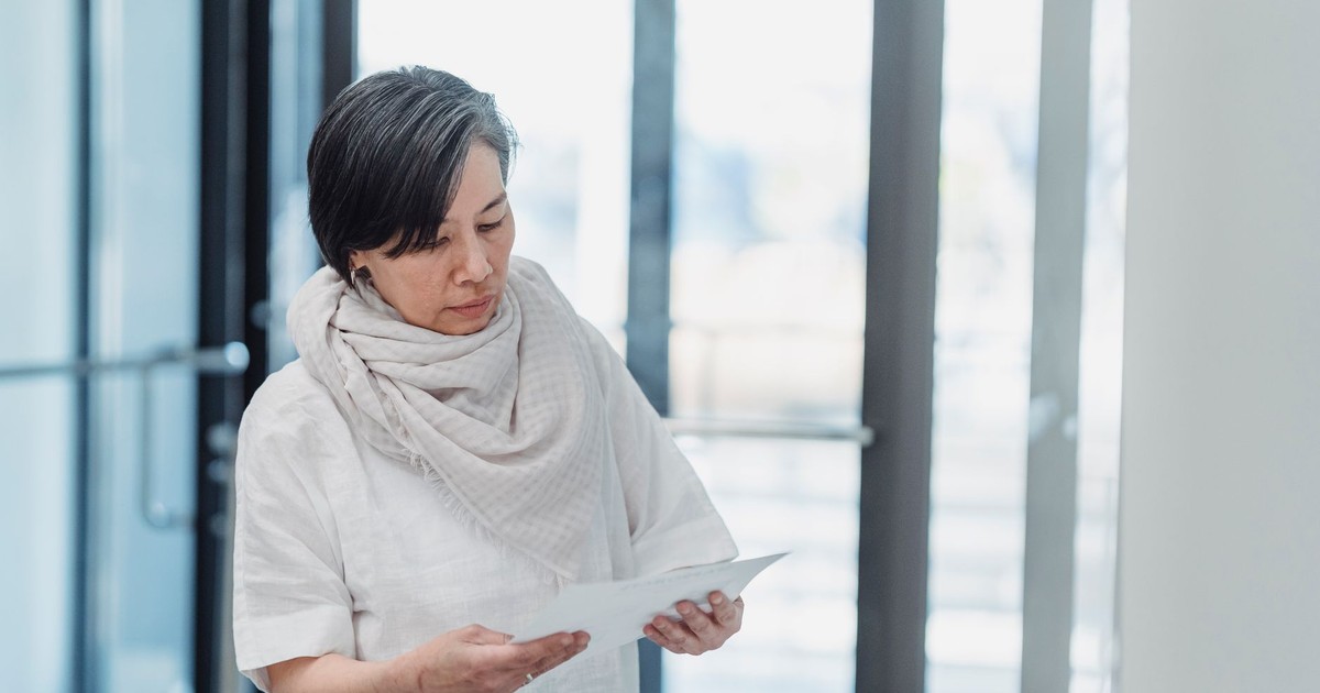 A senior woman reading papers in a bright office setting, exhibiting focus and concentration.