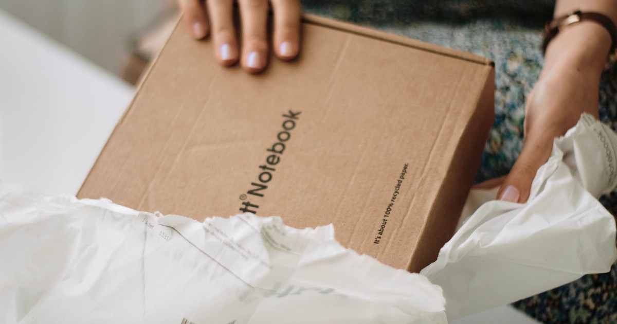 Woman unpacks a cardboard notebook in a cozy indoor setting, promoting eco-friendly packaging.