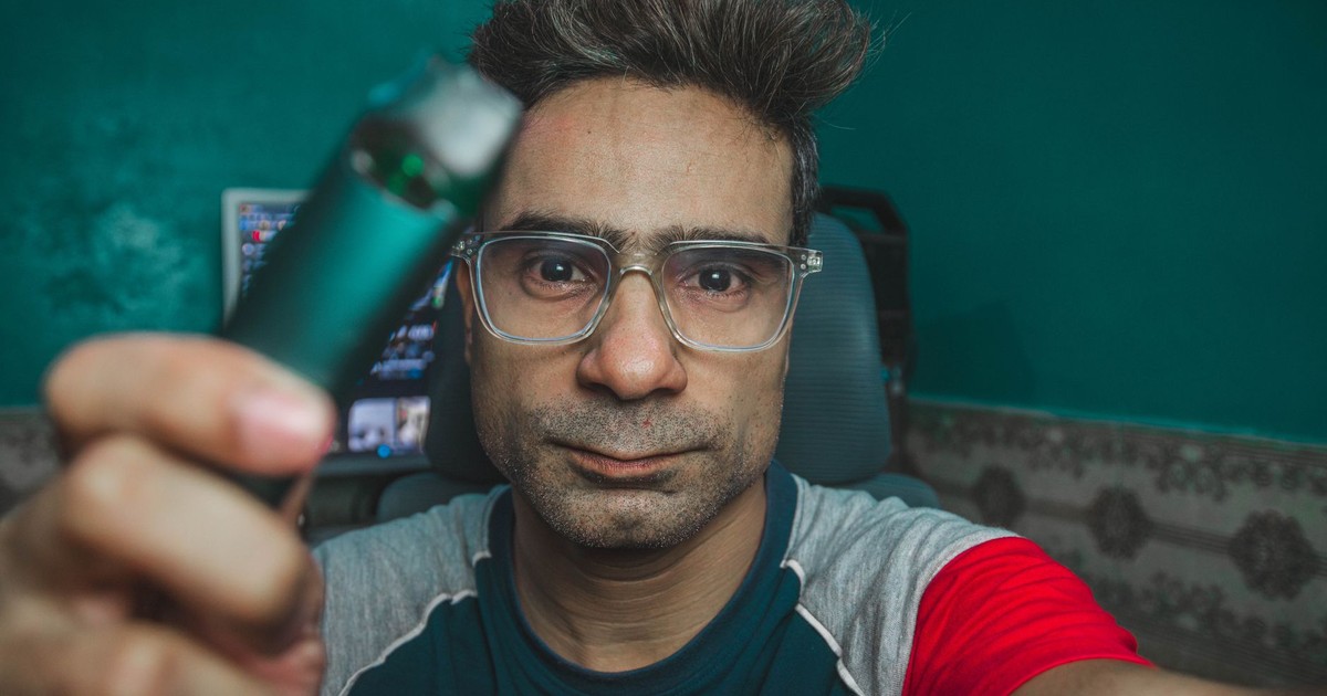 Close-up of a man wearing eyeglasses holding a vape pen, captured indoors.