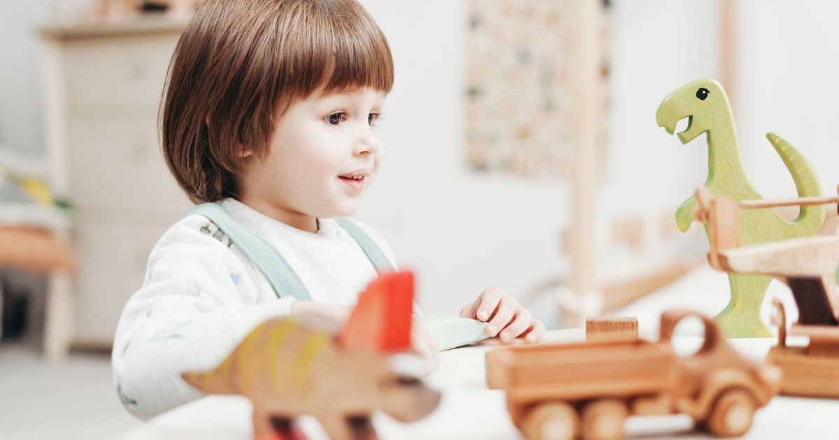 A happy child playing with wooden dinosaur toys in a bright playroom setting.