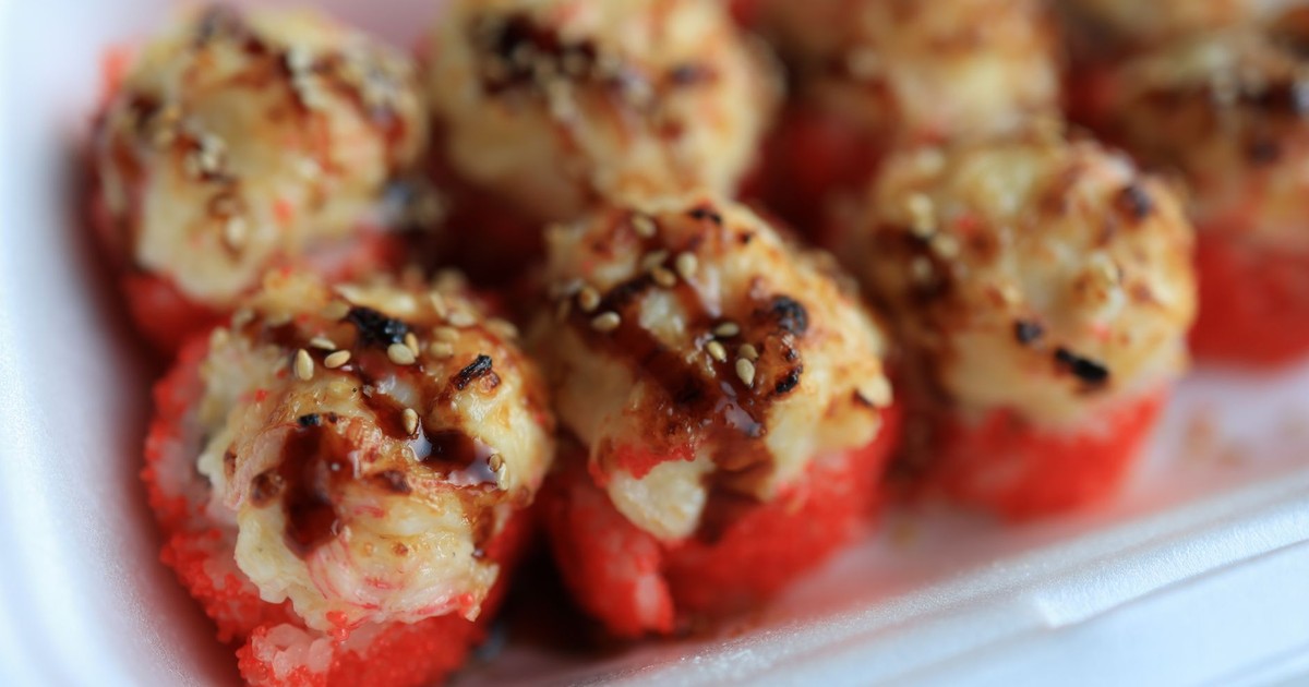 Delicious baked sushi rolls topped with sauce and sesame seeds in a styrofoam container, perfect for takeout.