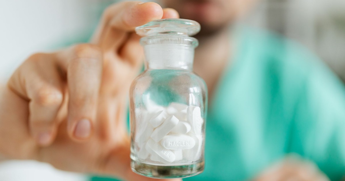 Crop medical worker in uniform holding in hand glass transparent bottle with white pills