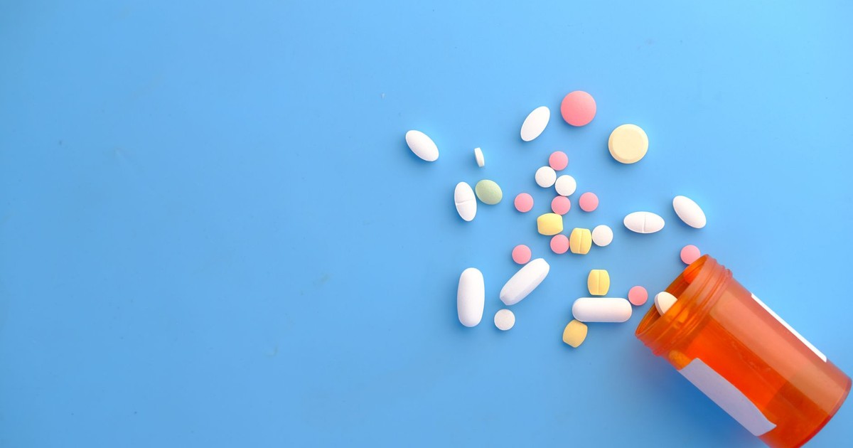 An assortment of colorful pills scattered from a prescription bottle on a blue background.