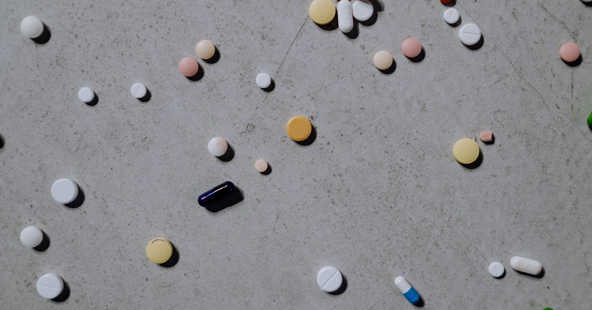 Varied colorful pills and tablets scattered on a grey surface, viewed from above.