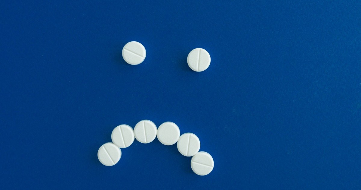White pills arranged in a sad face shape on a solid blue background.