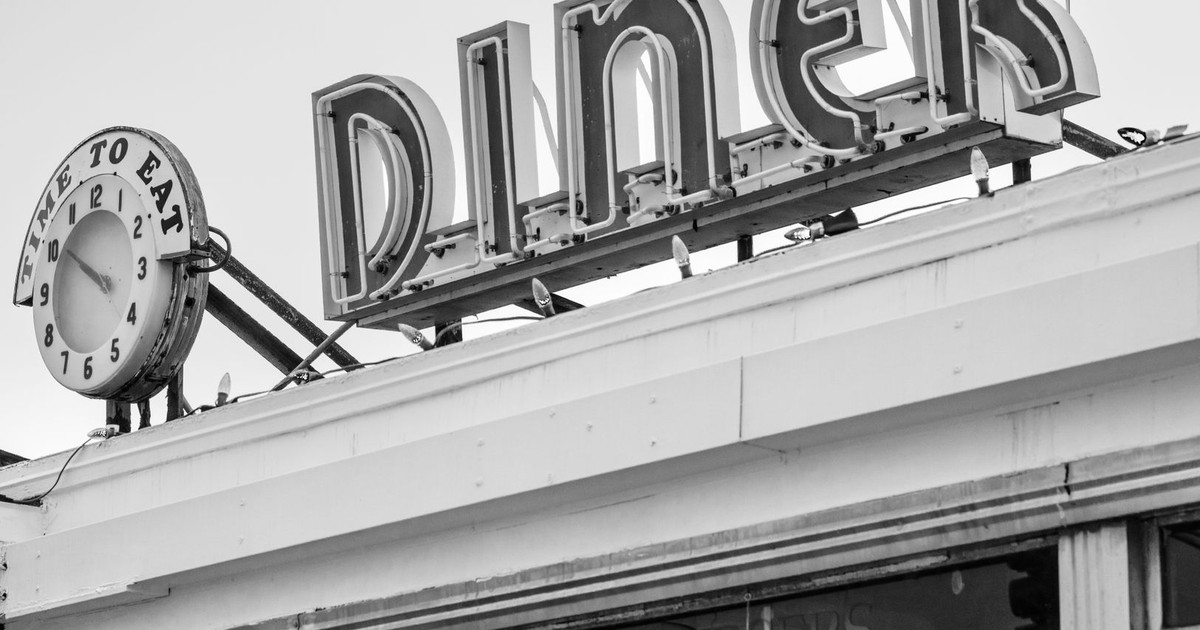 Black and white photo of a vintage diner sign with a clock in Somerville, MA.