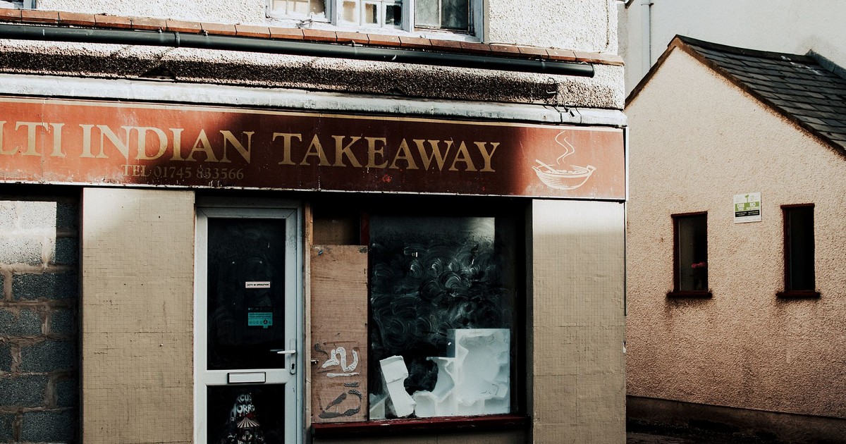 Exterior shot of an abandoned Indian takeaway restaurant with visible signage and boarded windows.