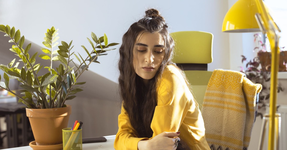 Woman in yellow sweater working in a sunlit office with plants.