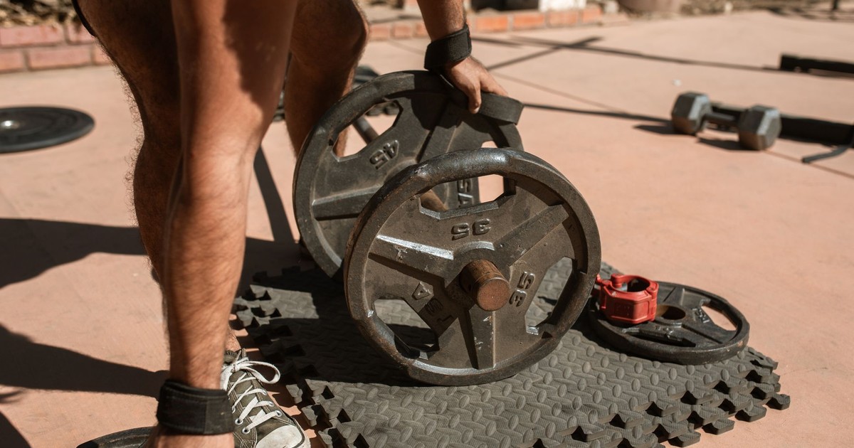 A man adjusts weight plates on a barbell during an outdoor workout session.