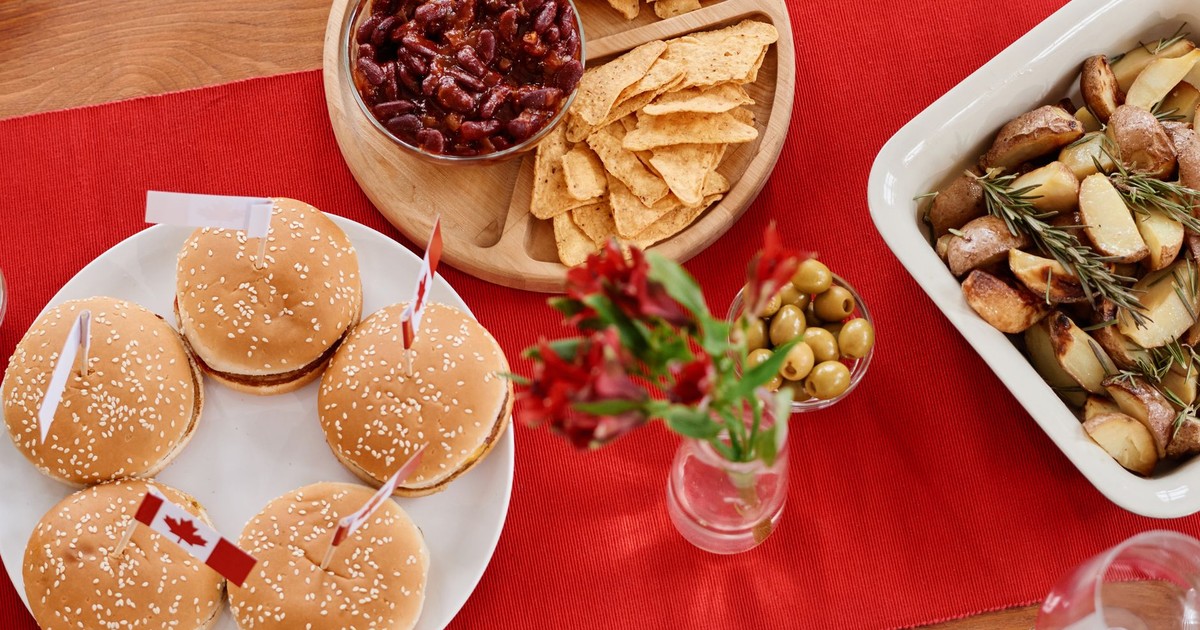 Top view of a festive Canadian-themed table with burgers, nachos, and roasted potatoes.