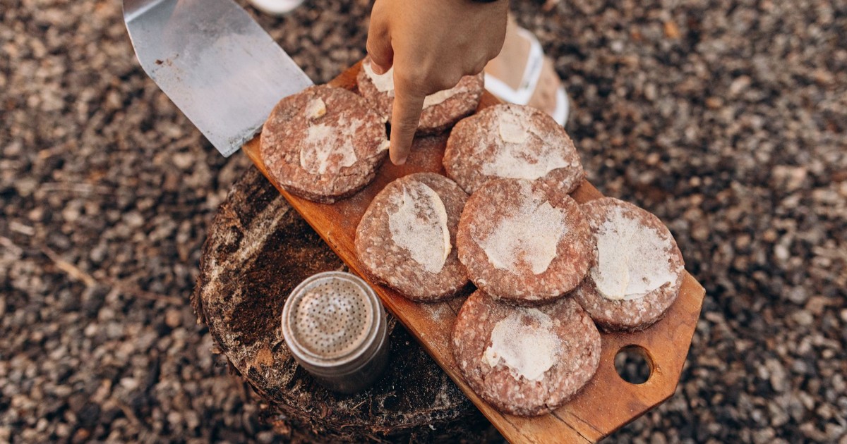 Close-up of hands preparing beef patties on cutting board, ready for grilling outdoors.