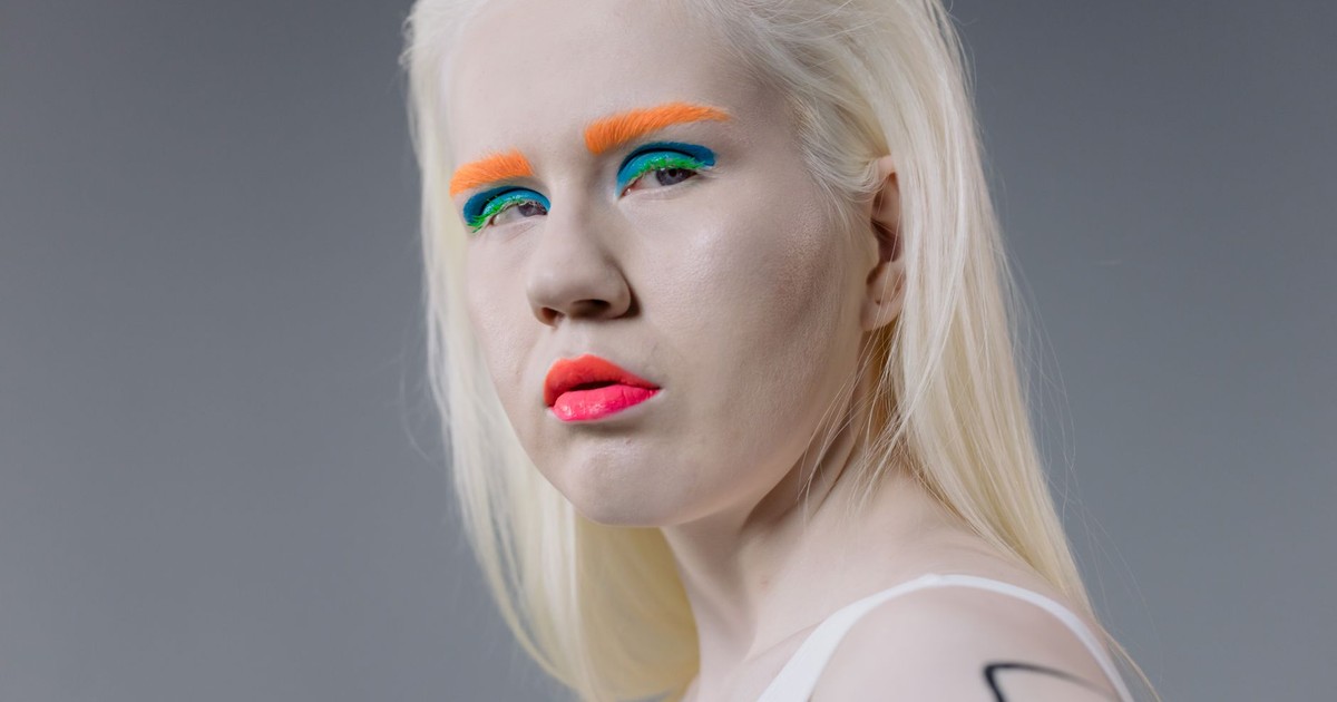 Portrait of an albino model with vibrant makeup and blond hair in a studio setting.