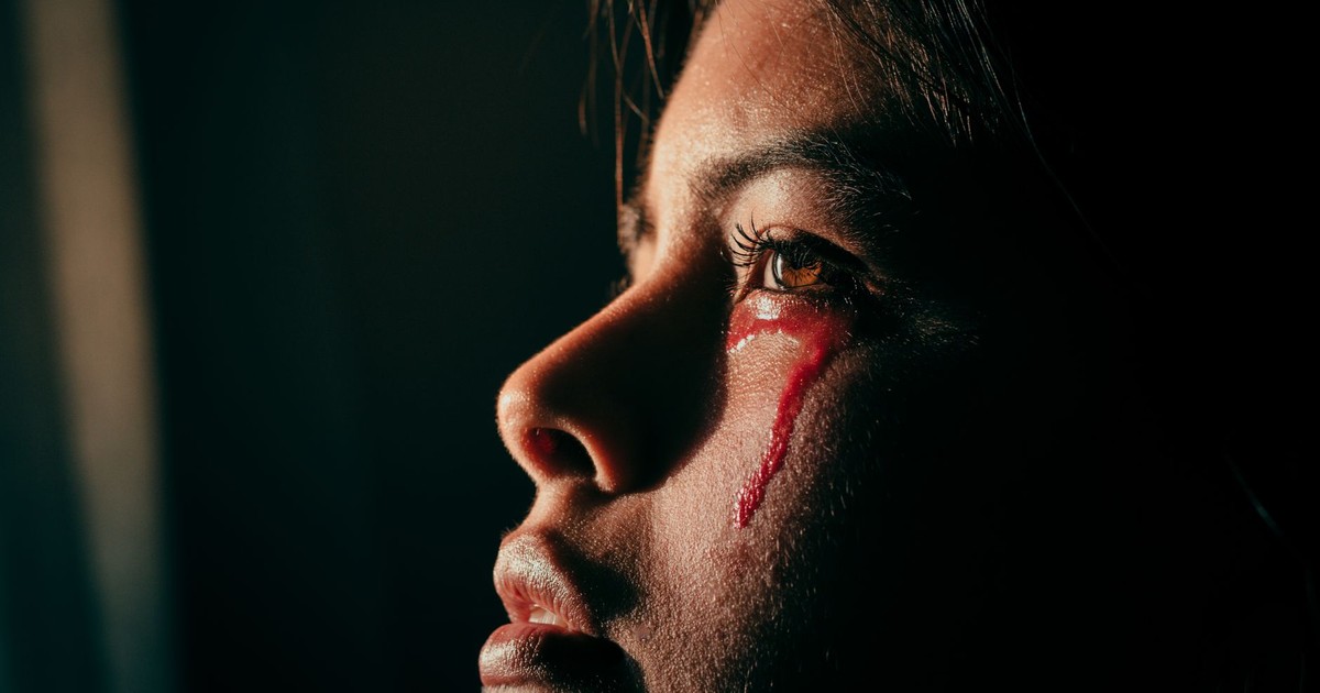 Close-up portrait of a woman with artistic light and red liquid resembling tears, evoking emotion and sorrow.