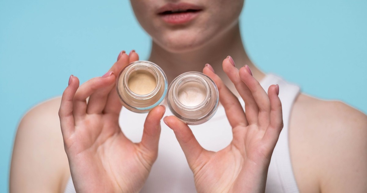 Close-up of a woman holding skincare jars against a blue background, showcasing beauty and self-care.