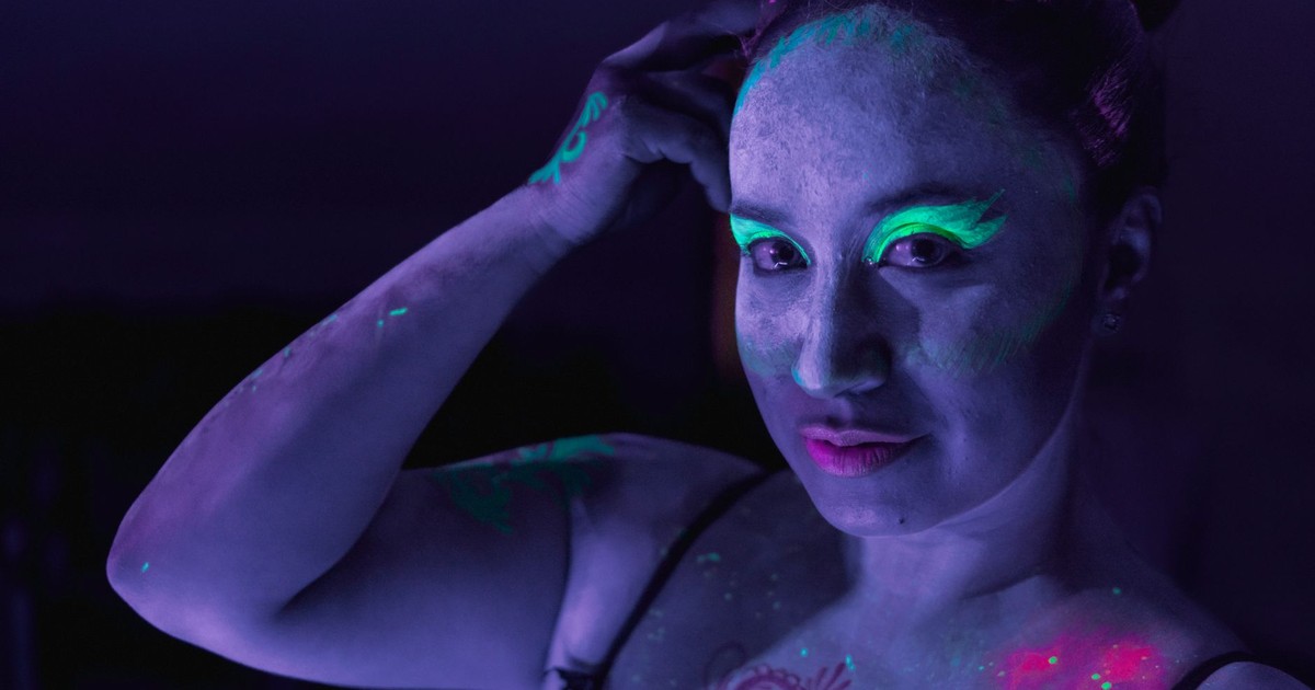 Portrait of a woman with neon makeup glowing under ultraviolet light in a dark room.
