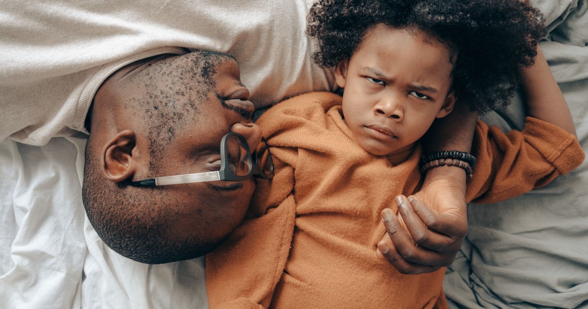 Top view of African American man in glasses lying near angry child in casual clothes while cuddling together in comfortable bedroom