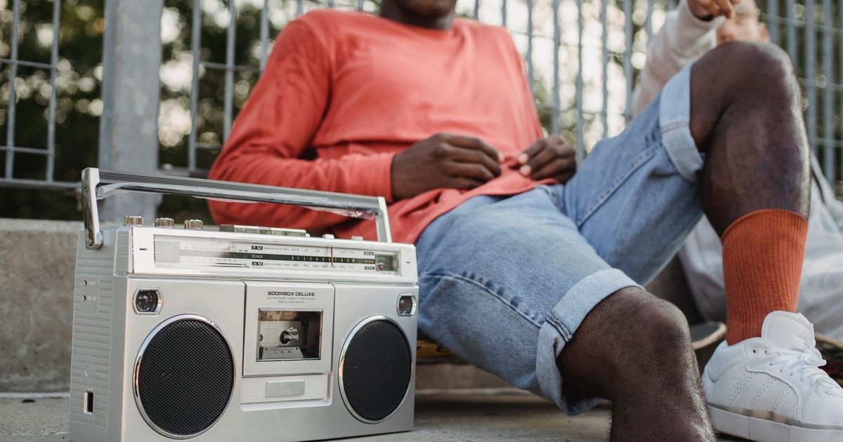 Crop anonymous multiracial friends skaters resting on street with retro portable stereo boombox radio cassette recorder in daytime