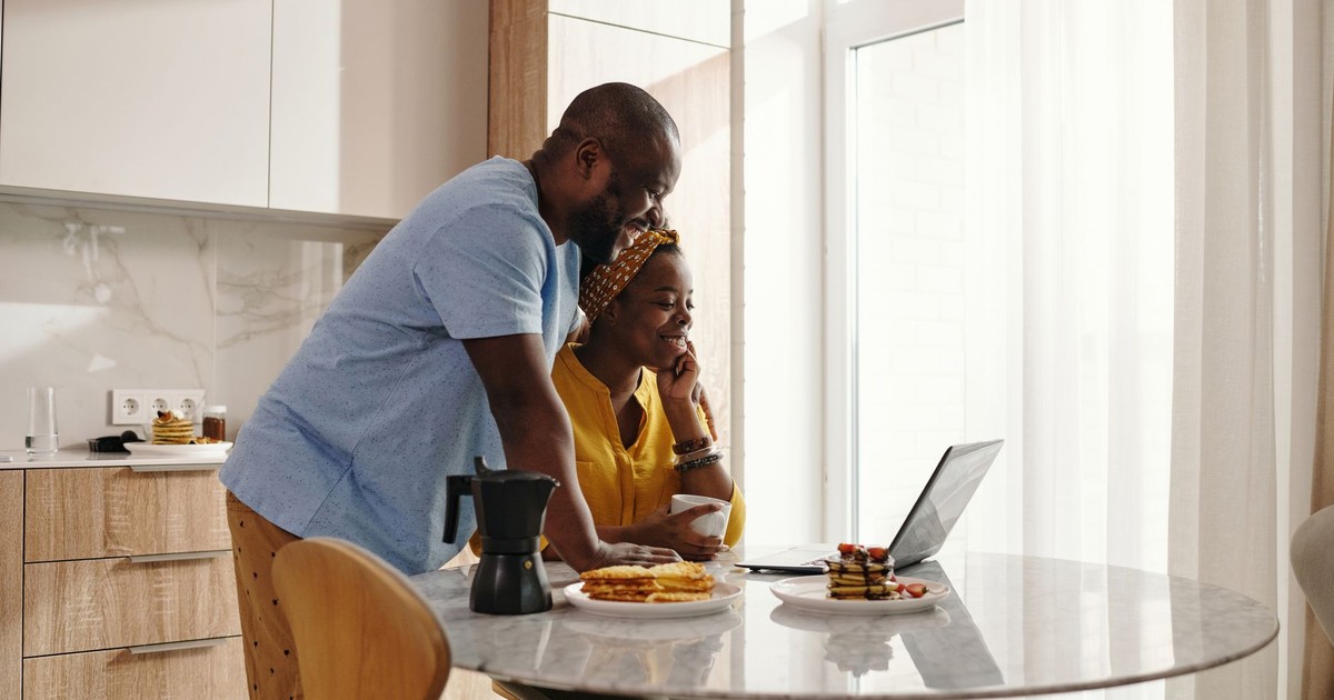 A joyful couple sharing breakfast and working on a laptop in their cozy kitchen.