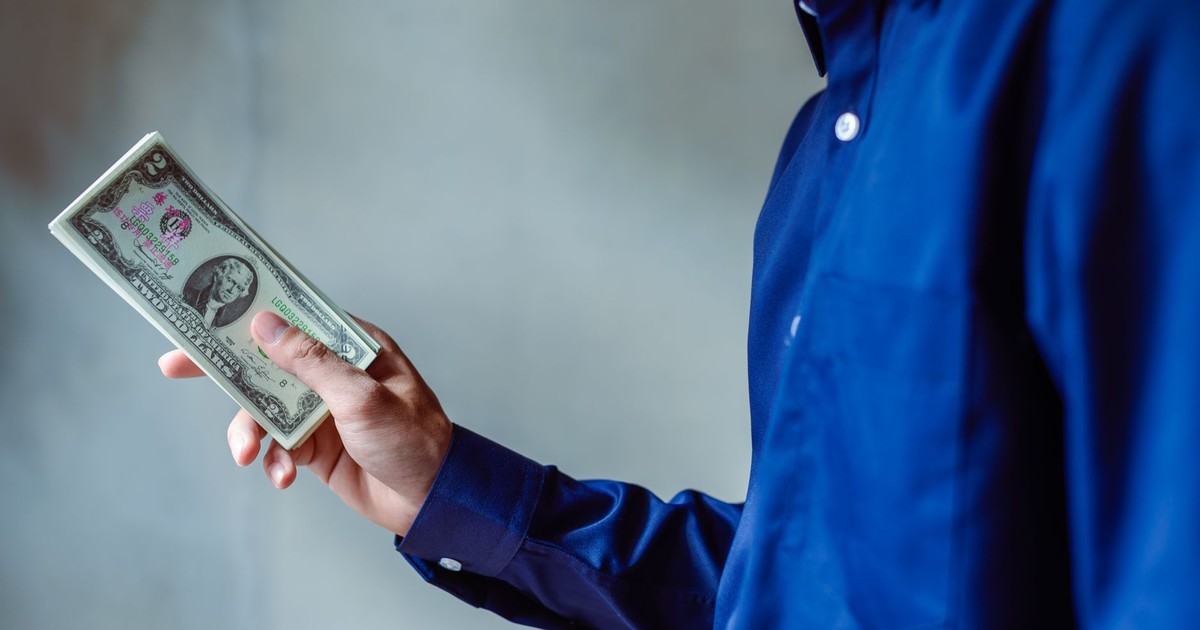 A person in a blue shirt holding a stack of US dollar bills, symbolizing wealth and finance.