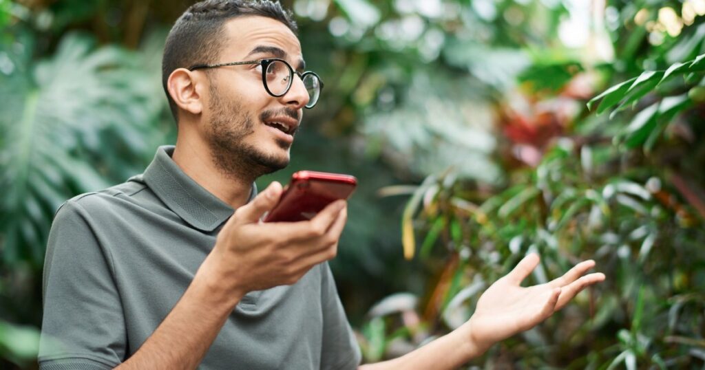 Man talking on smartphone in lush outdoor setting, expressing emotion