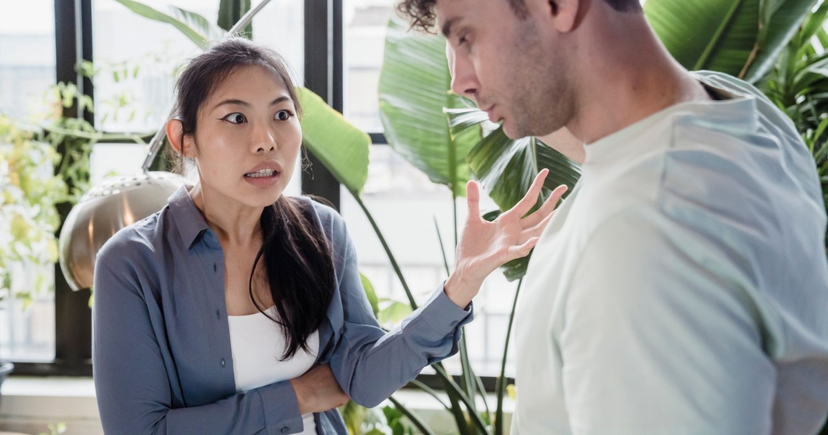 A couple engaged in a heated discussion indoors surrounded by plants, expressing emotions.