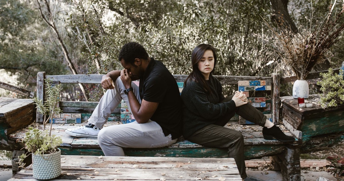 A couple sits back to back on a wooden bench, indicating a disagreement or breakup.