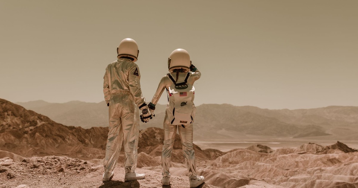 Two astronauts in space suits holding hands in a desert, Mars-like terrain.