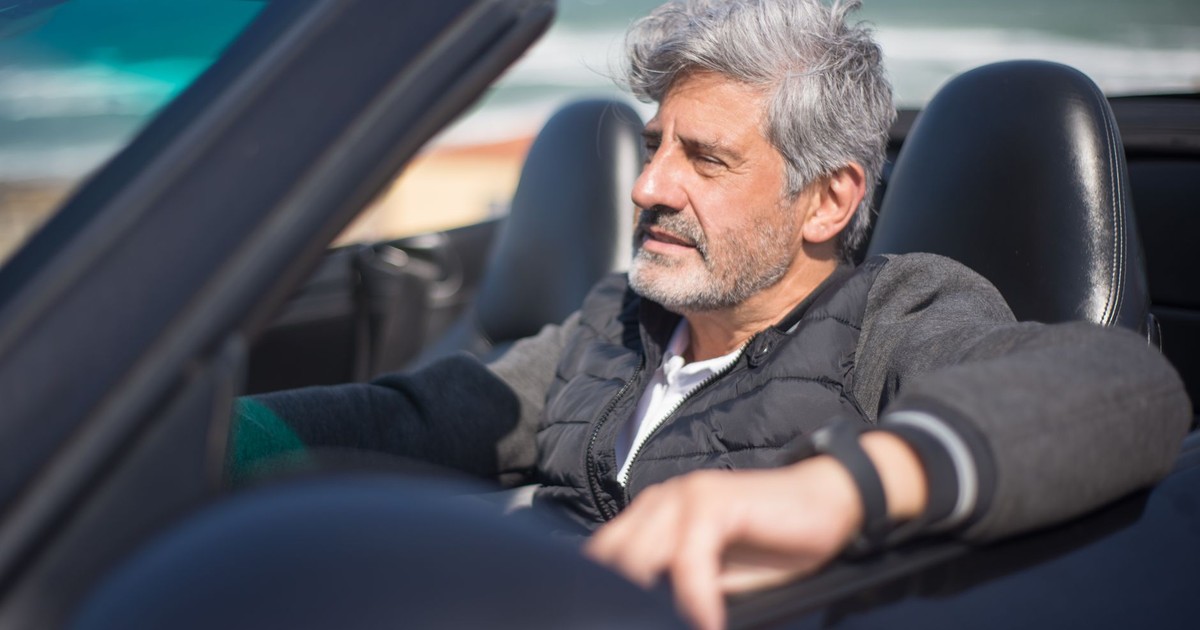 Senior man enjoying a road trip along a scenic coastal drive in a convertible car.