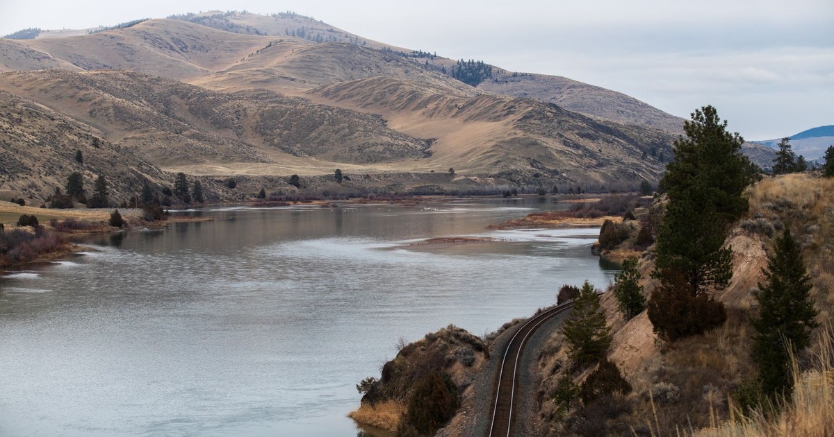 Peaceful river with mountains and railway in Montana's natural landscape.